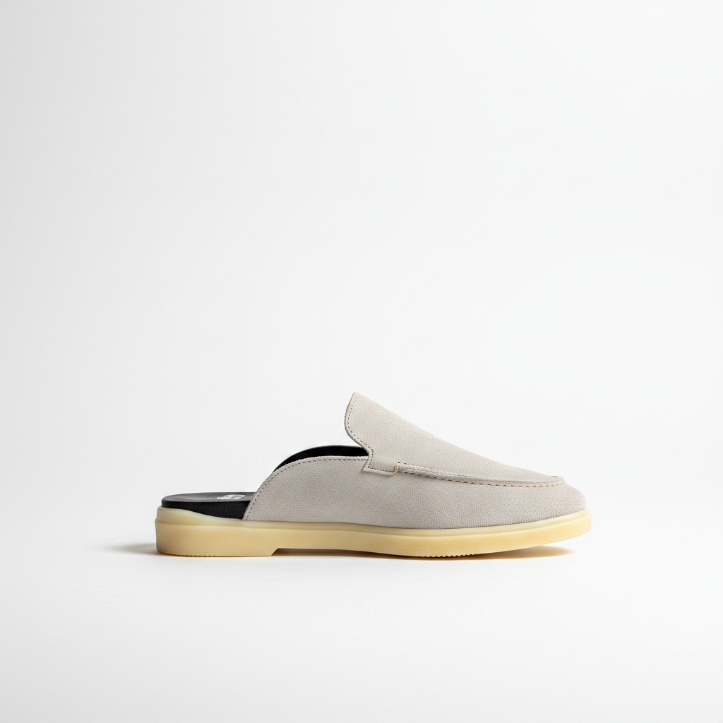 A light gray suede slip-on mule shoe with a black insole and a beige gum sole, shown from a side profile on a clean white background.