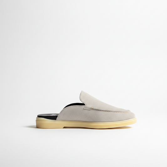 A light gray suede slip-on mule shoe with a black insole and a beige gum sole, shown from a side profile on a clean white background.