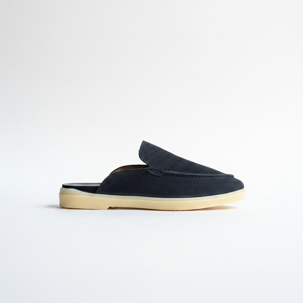 A single slip-on loafer mule in dark navy suede with a thick, light beige gum sole, shown in profile against a clean white background.
