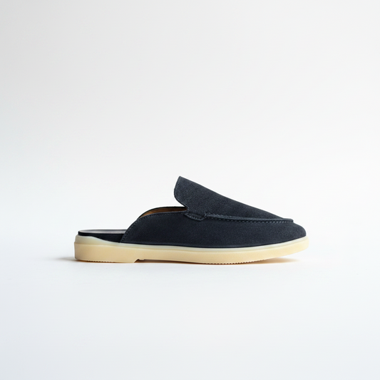 A single slip-on loafer mule in dark navy suede with a thick, light beige gum sole, shown in profile against a clean white background.