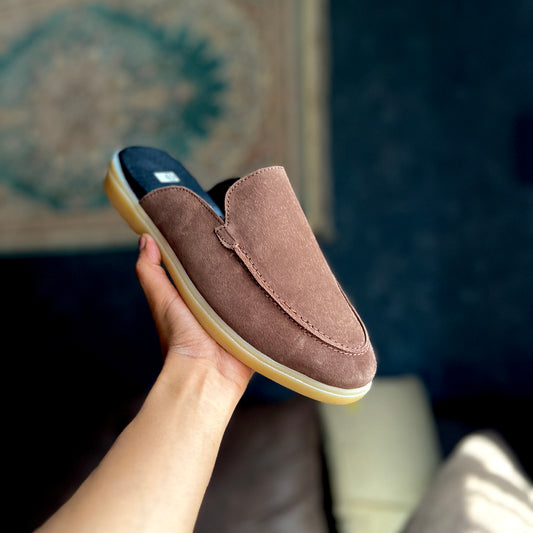 Brown suede slip-on shoe held by a hand with a blurred background