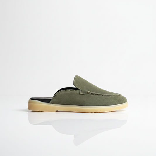 An olive green suede slip-on mule shoe with a light beige sole, shown in profile against a clean white background with a soft reflection below.